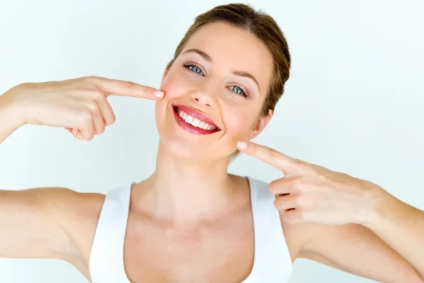 Confident woman smiling and pointing to her face, representing restored self-esteem through paramedical tattooing.