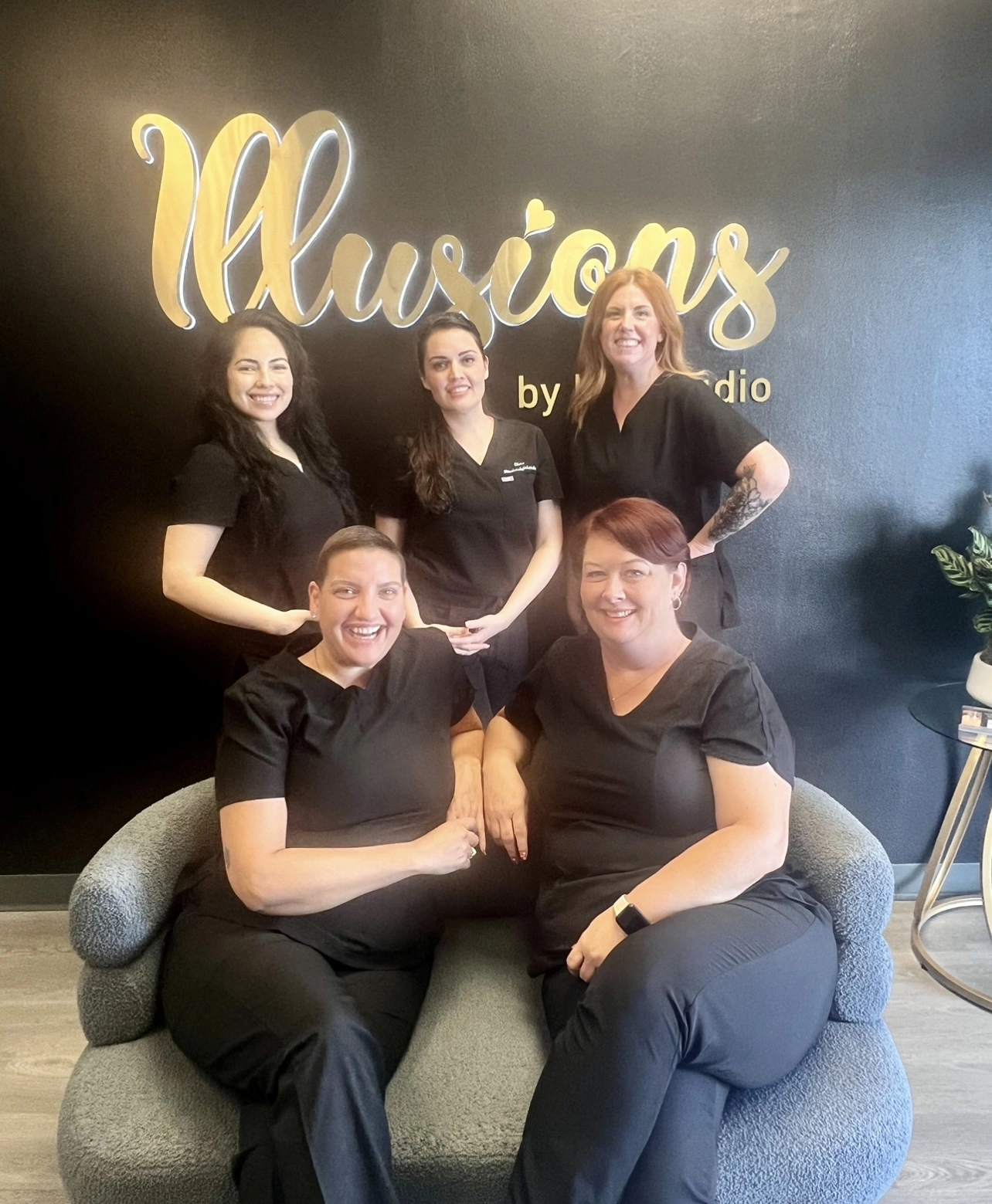 Elena Sanchez with her scar camouflage tattoo group training class at Illusions by Ink Studio, students in professional uniforms posing in front of the studio logo.